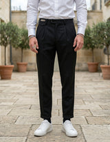 Close-up front view of male model wearing black pleated tailored pants with a relaxed straight-leg fit.