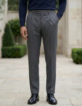 Close-up front view of male model wearing dark gray pleated tailored pants with a slim straight-leg fit.