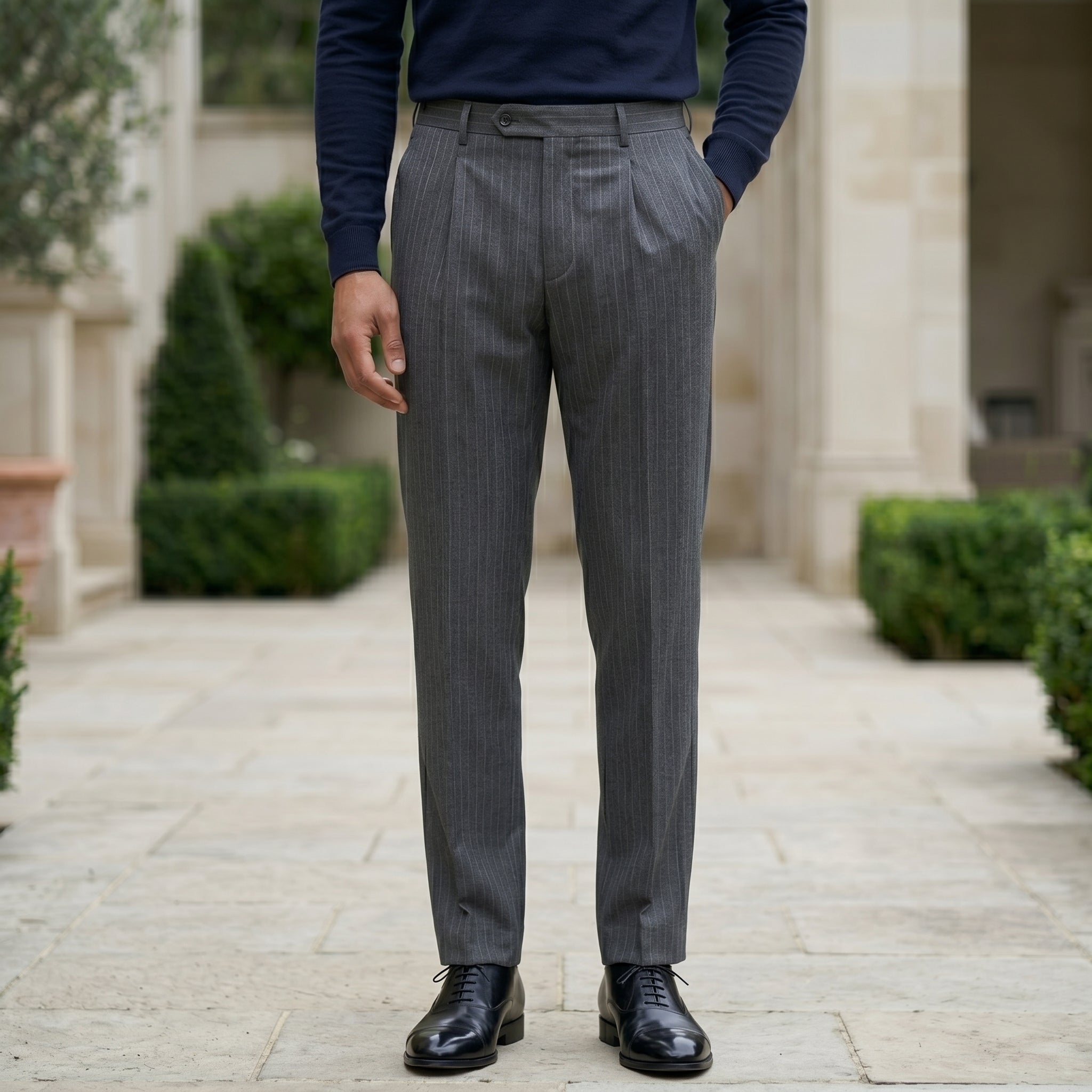 Close-up front view of male model wearing dark gray pleated tailored pants with a slim straight-leg fit.