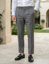 Close-up front view of male model wearing gray pleated tailored pants with a slim straight-leg fit.