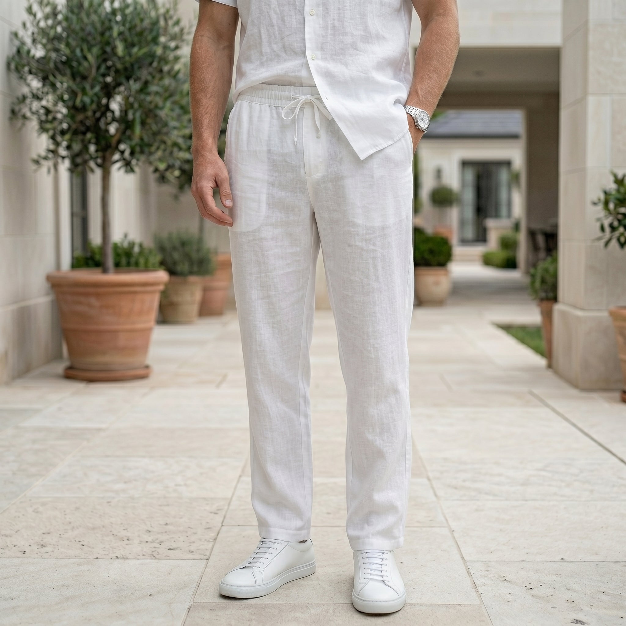 Close-up front view of male model wearing white drawstring relaxed-fit pants with a white short-sleeve shirt.