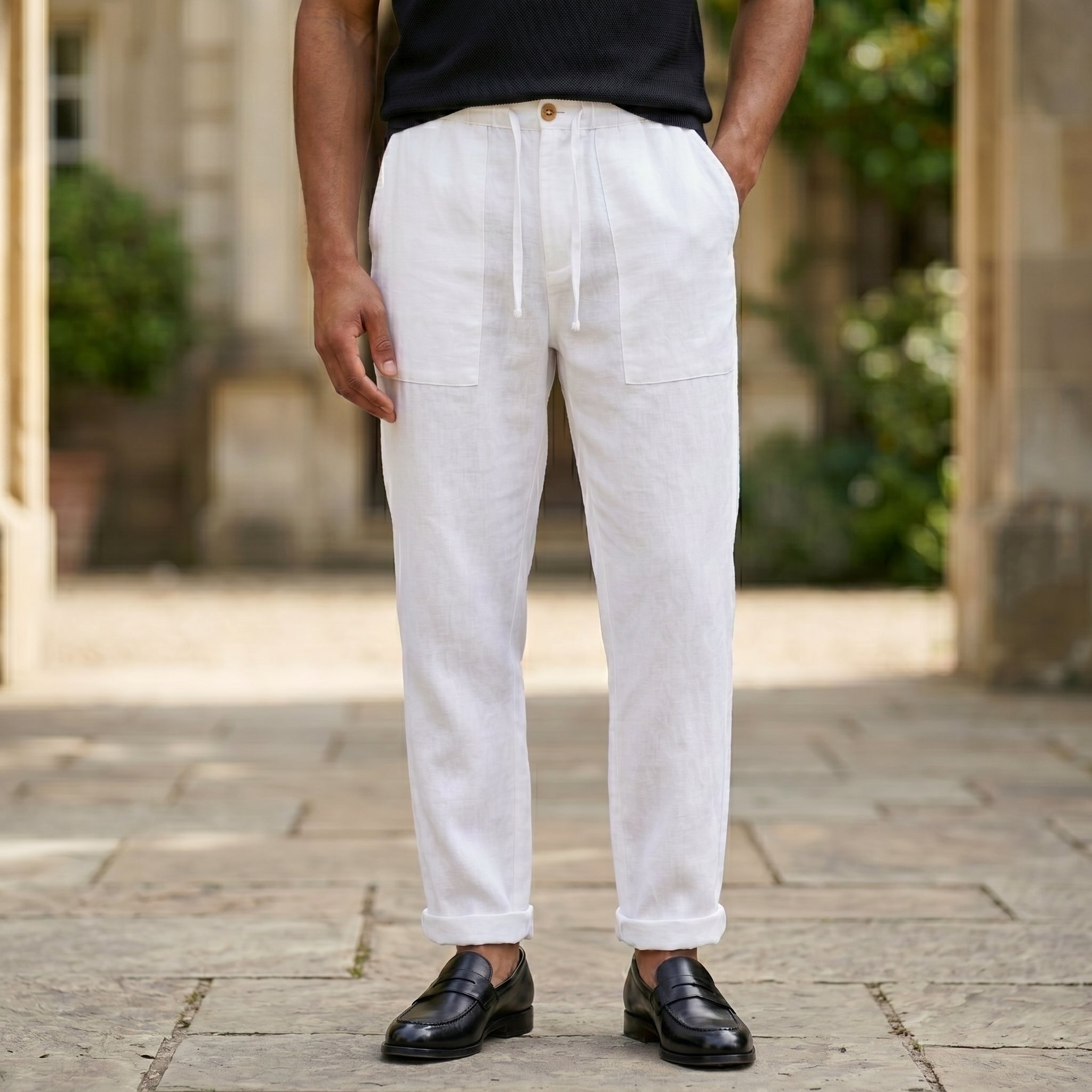 Close-up front view of male model wearing white relaxed-fit pants with a black short-sleeve polo shirt.