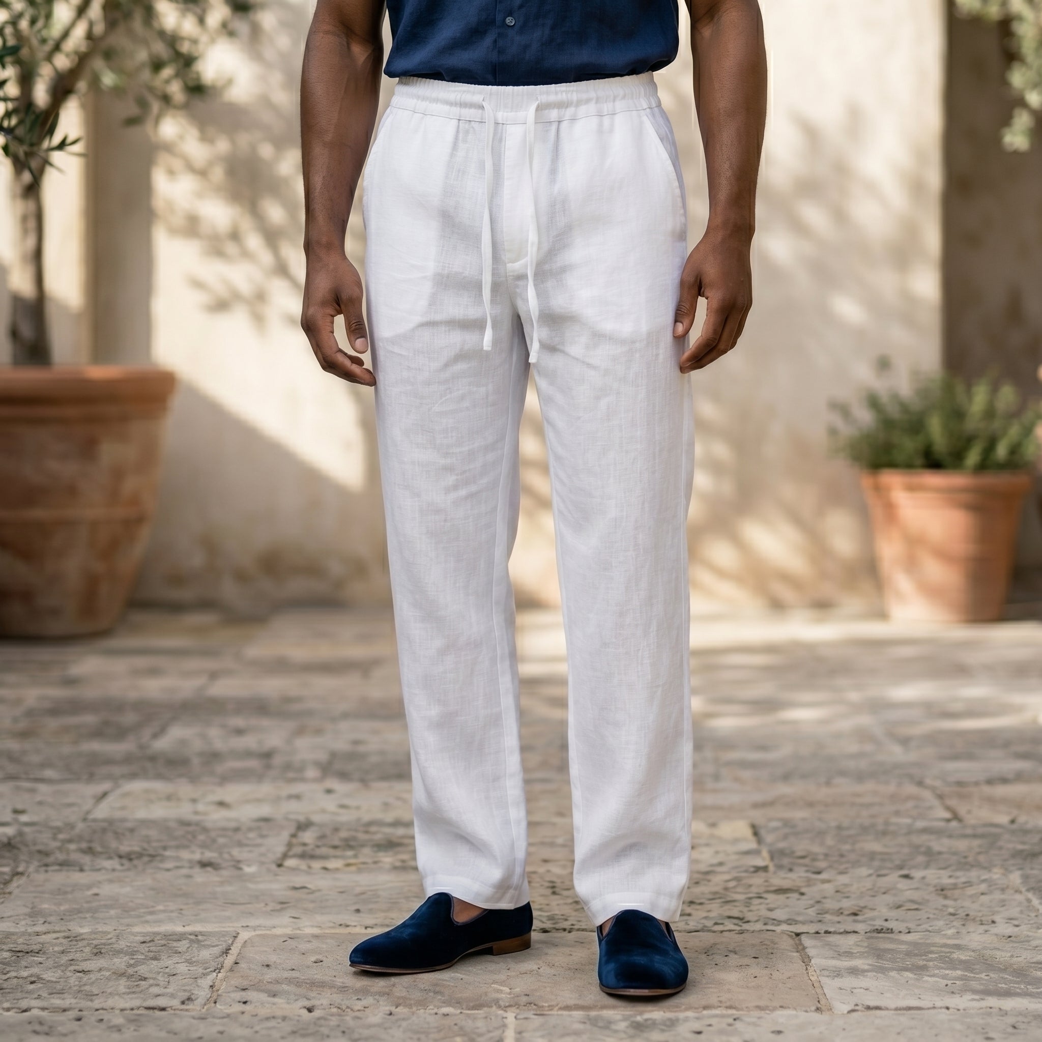 Close-up front view of male model wearing white relaxed-fit pants with a navy short-sleeve button-up shirt.