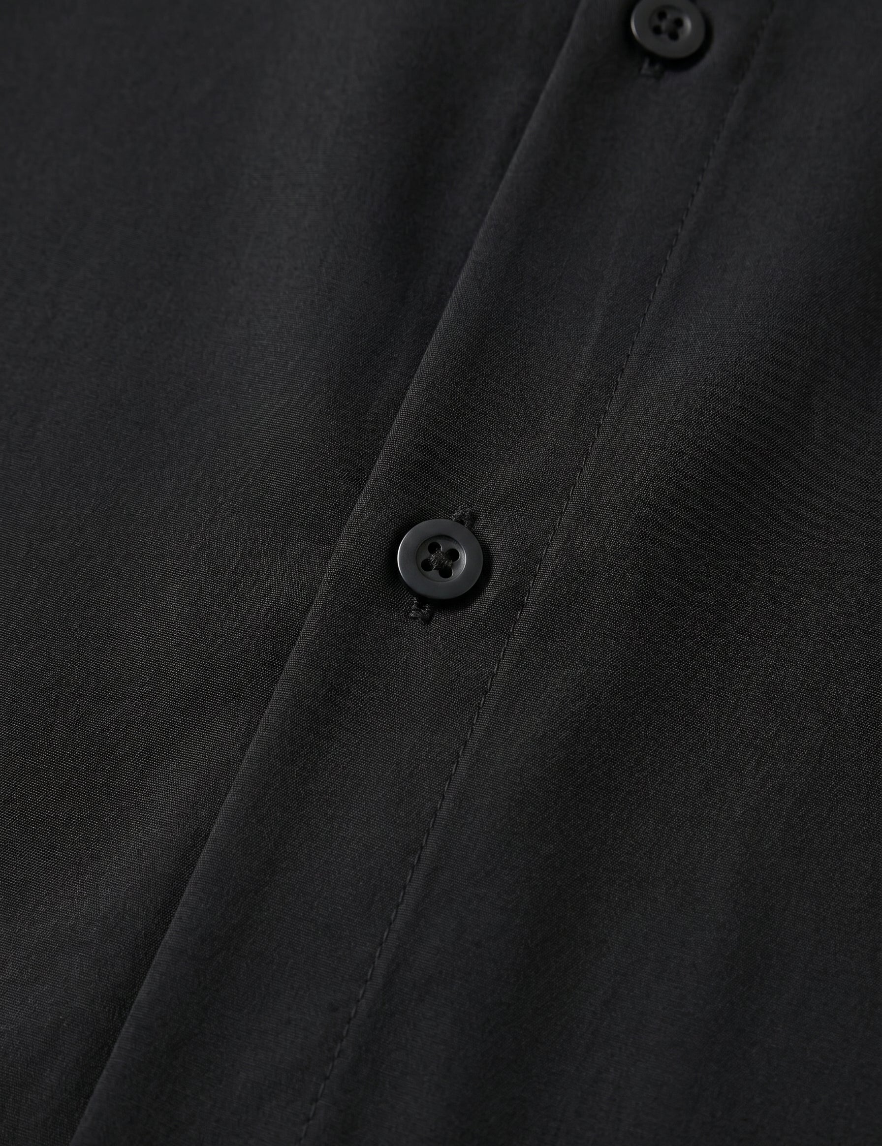 Close-up of a black buttoned shirt with a focus on texture and buttons.