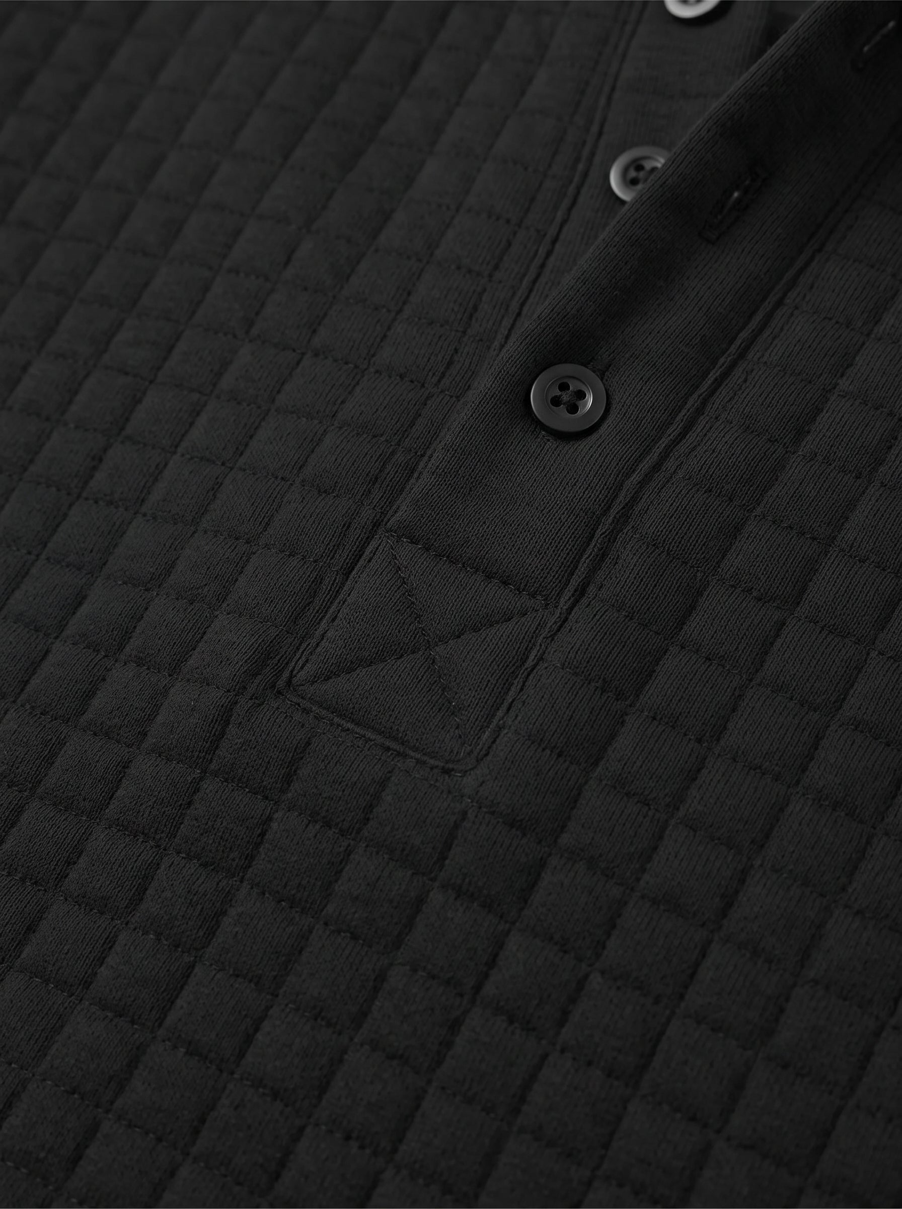 Close-up of a black quilted long-sleeve top showing the diamond-stitched texture and a button placket.