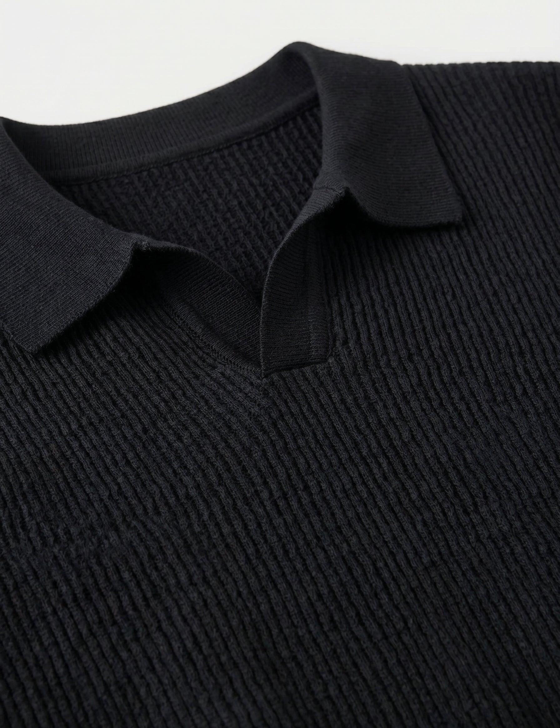 Close-up of a black ribbed sweater with a collar on a light gray background