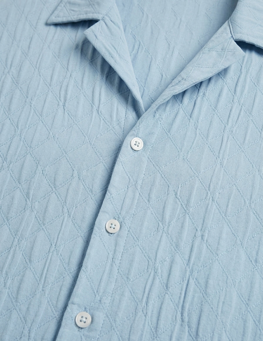 Close-up of a light blue textured shirt with buttons.
