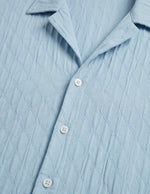 Close-up of a light blue textured shirt with buttons.
