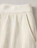 Close-up of a pleated cream skirt against a neutral background