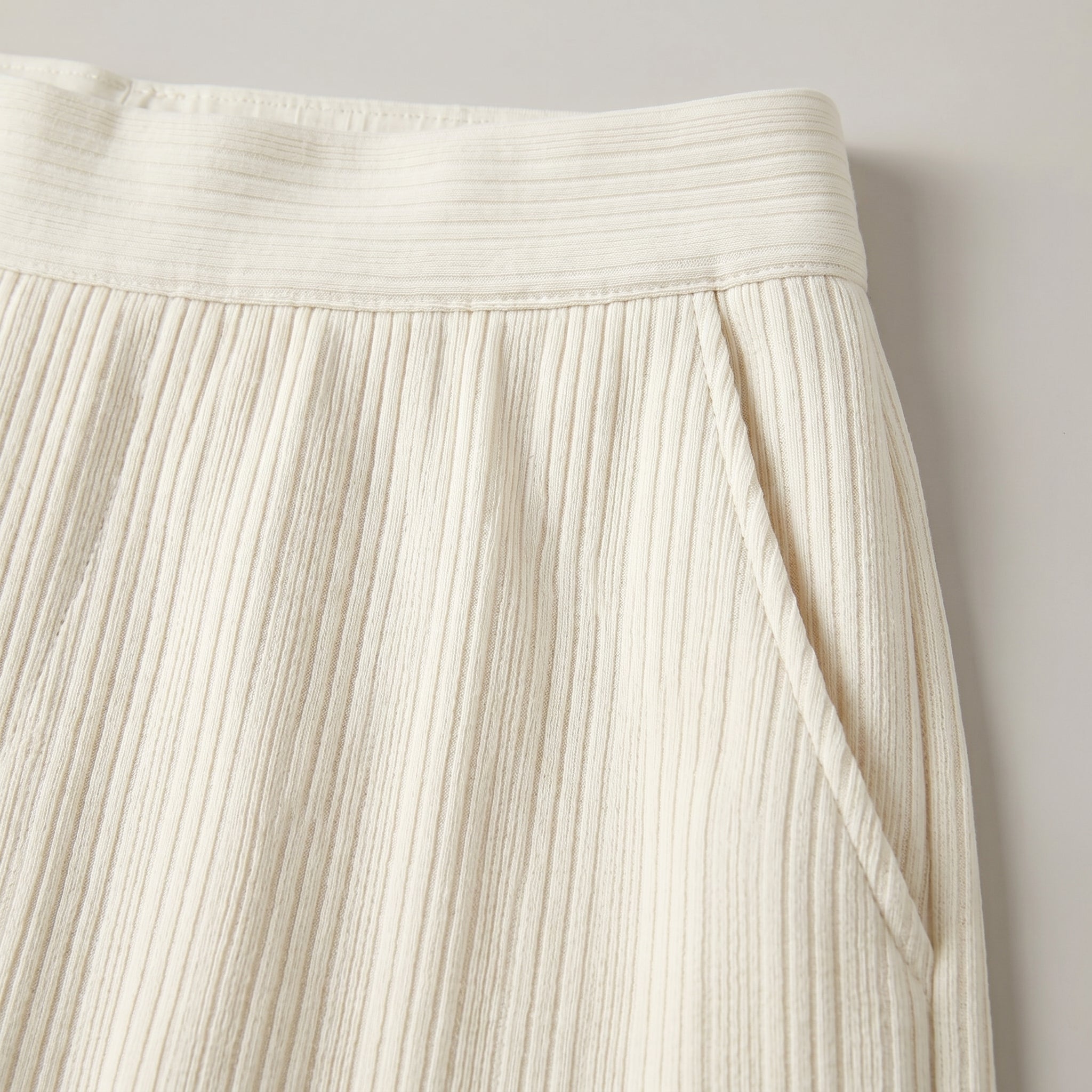 Close-up of a pleated cream skirt against a neutral background