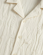 Close-up of a textured cream-colored shirt with buttons.