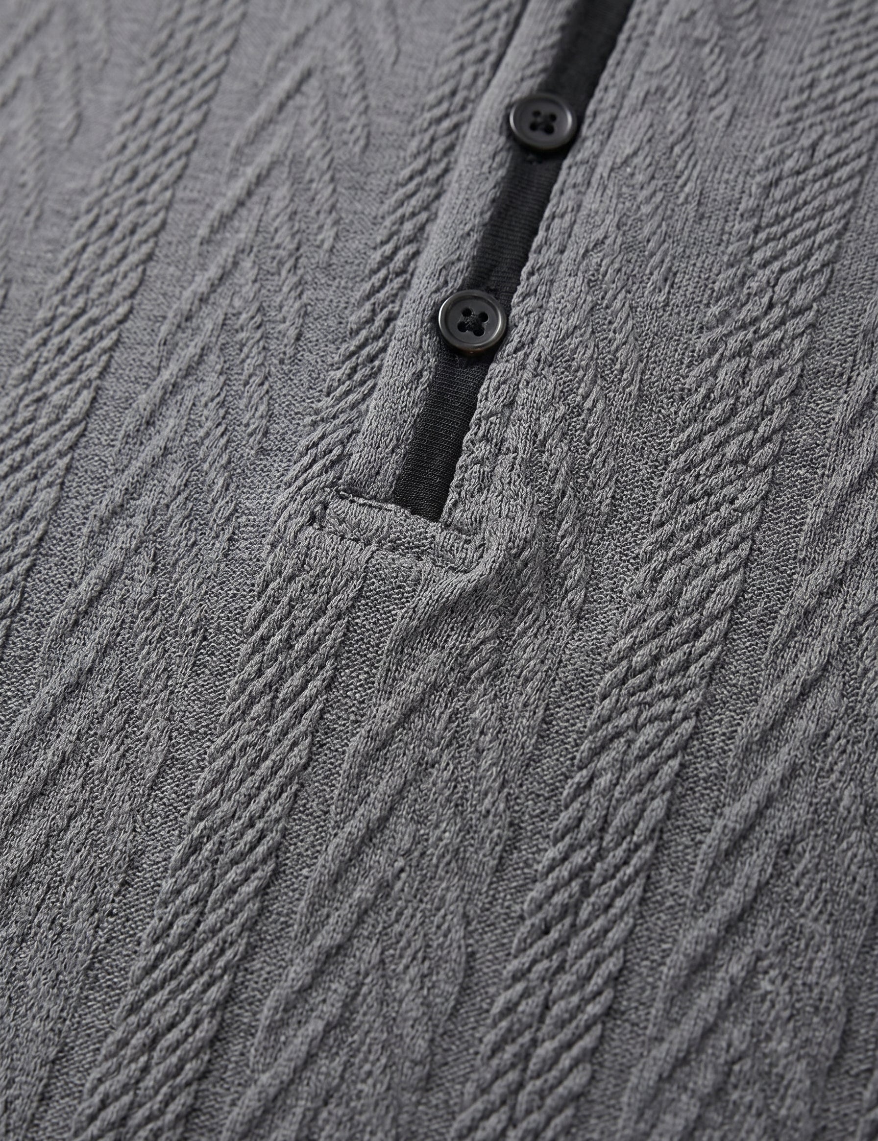 Close-up of a textured gray garment with buttons and a black strap.