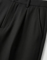 Close-up of black pleated pants on a light gray background