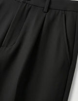 Close-up of black pleated pants on a light gray background