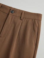 Close-up of brown pleated pants on a light gray background