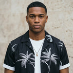 Close-up of male model wearing a black palm print short-sleeve summer shirt over a white T-shirt.