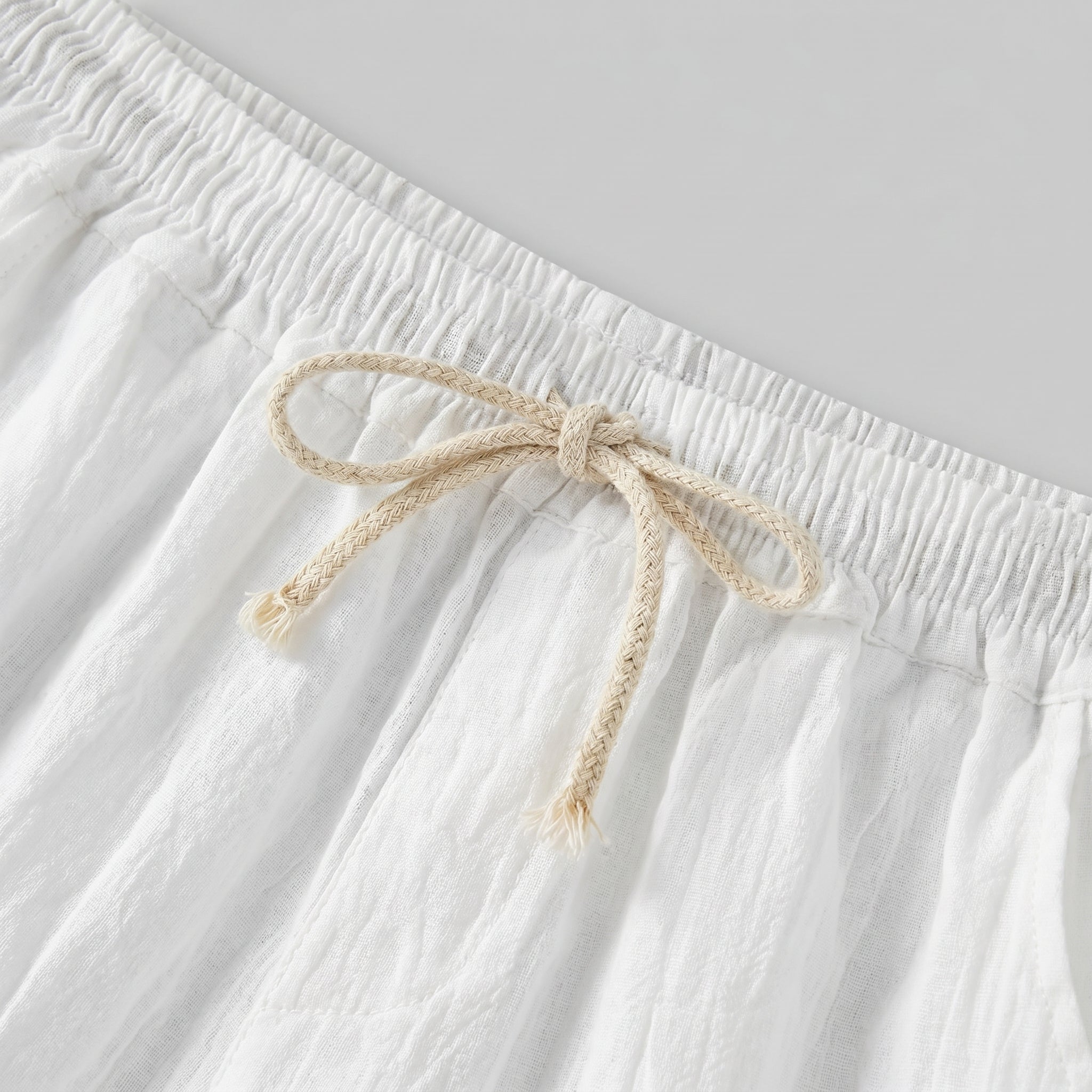 Close-up of white textured drawstring summer shorts with elastic waistband and beige rope tie.