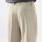 Close-up side view of beige pleated casual pants showing the relaxed fit and front pleats.