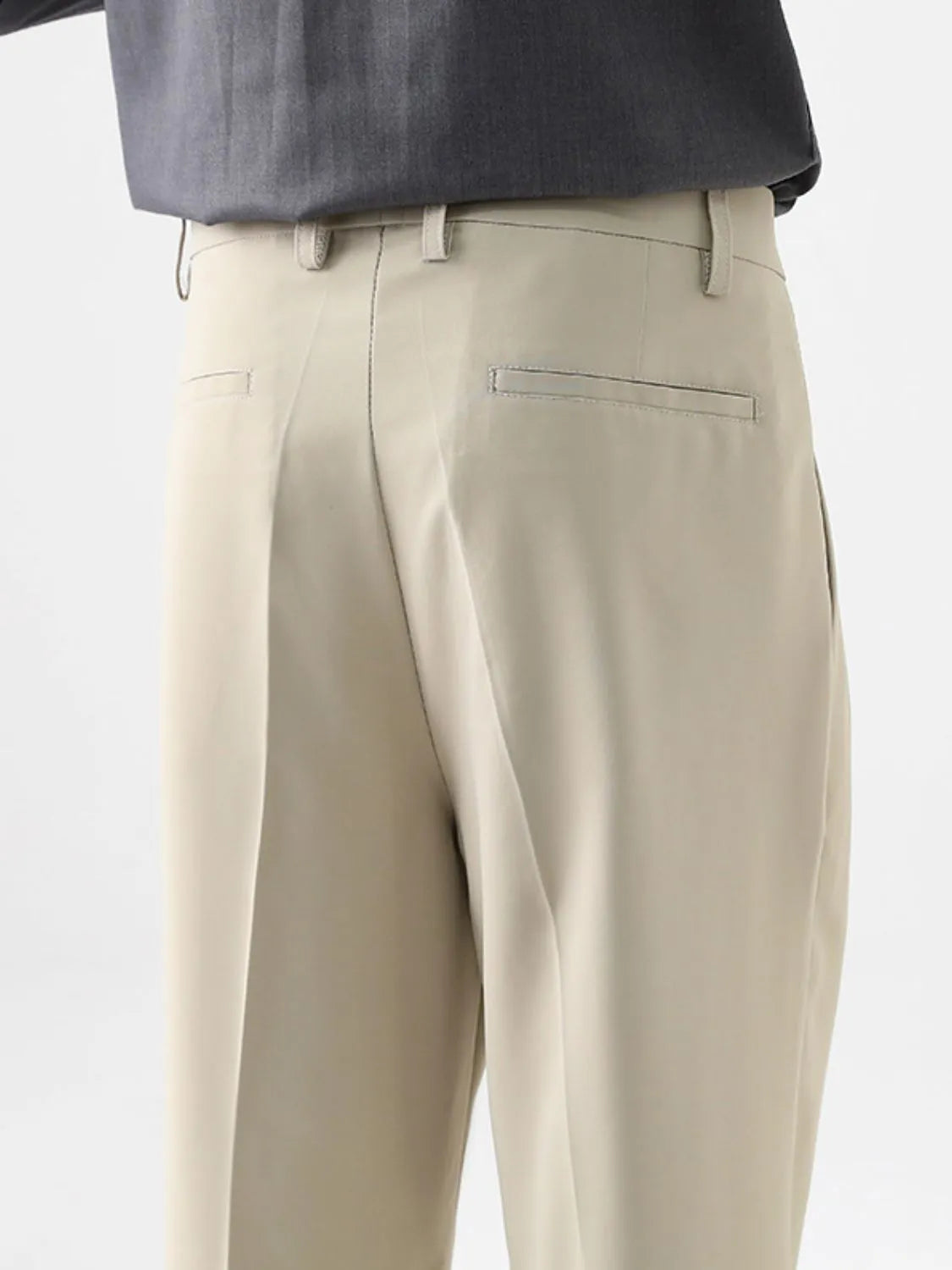 Close-up side view of beige pleated casual pants showing the relaxed fit and front pleats.