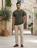 Man wearing a green t-shirt and beige pants standing in front of a stone building with potted plants.