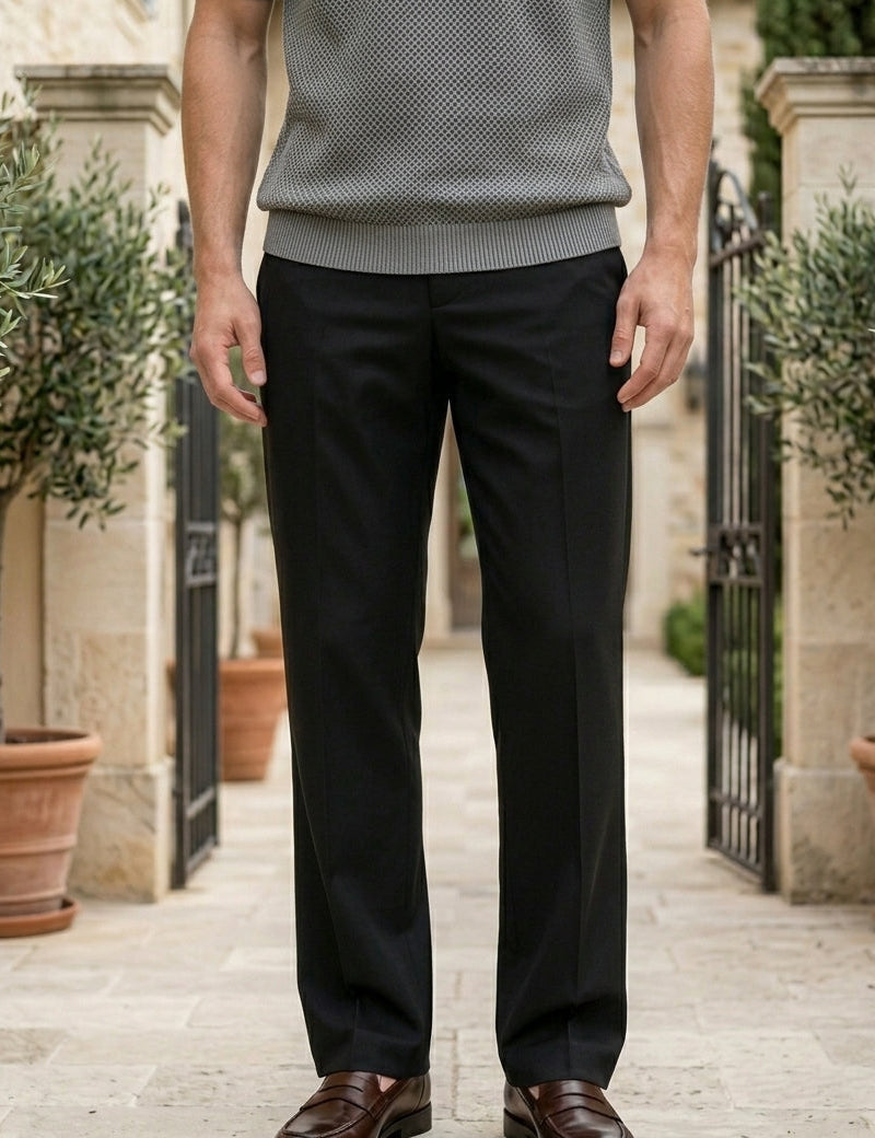 Person wearing a gray sweater and black pants standing outdoors with potted plants and a building in the background.
