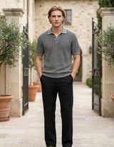 Graphite - Man wearing a gray polo shirt and black pants standing in an outdoor setting with stone walls and potted plants.