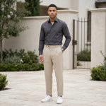 Male model wearing beige pleated casual pants with a dark gray long-sleeve shirt in an outdoor walkway setting.