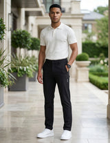 Male model wearing black casual pants with a white short-sleeve polo shirt in an outdoor walkway setting.