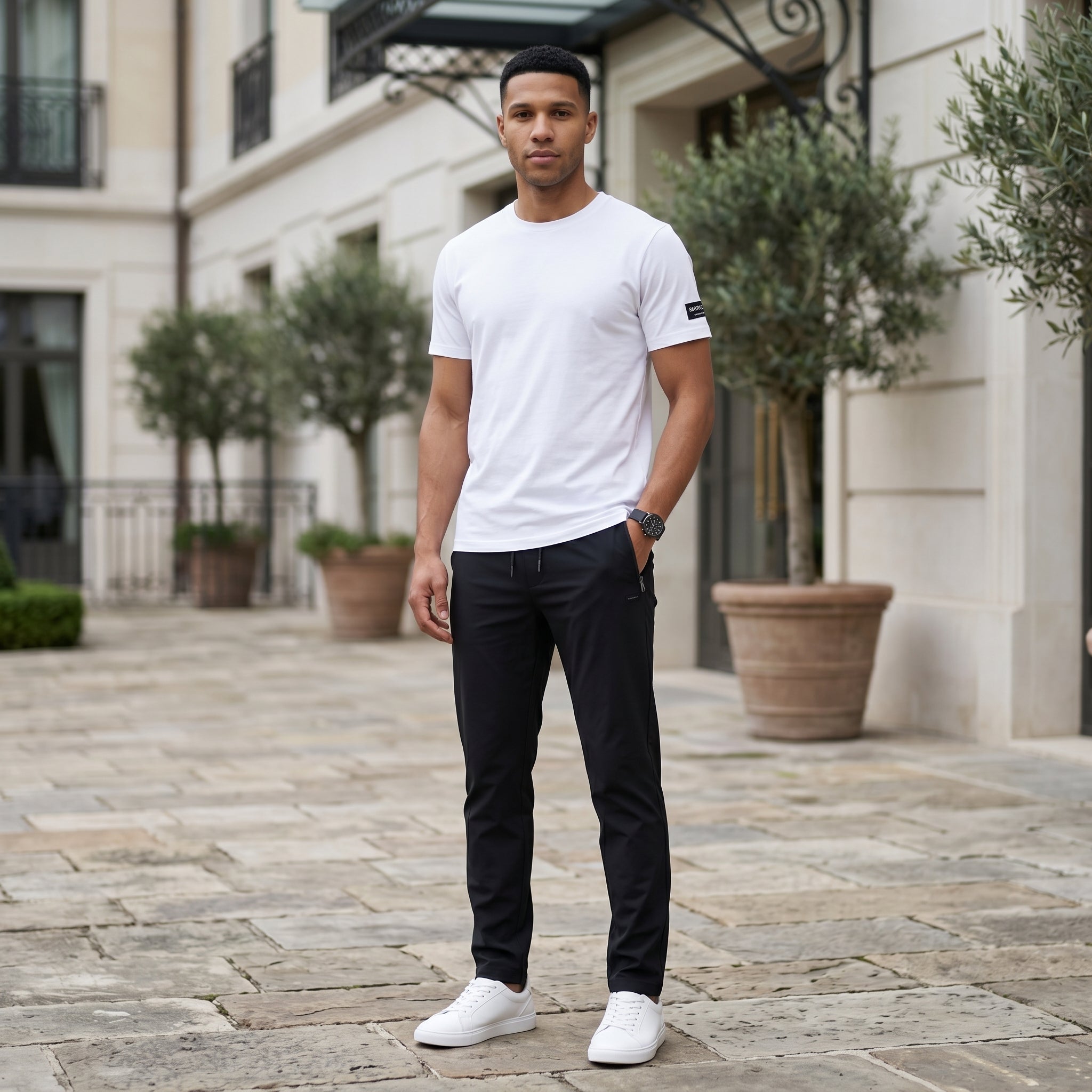 Male model wearing black jogger pants with a white T-shirt in an outdoor stone walkway setting.
