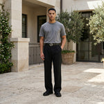 Male model wearing black pleated casual pants with a gray T-shirt in an outdoor walkway setting.