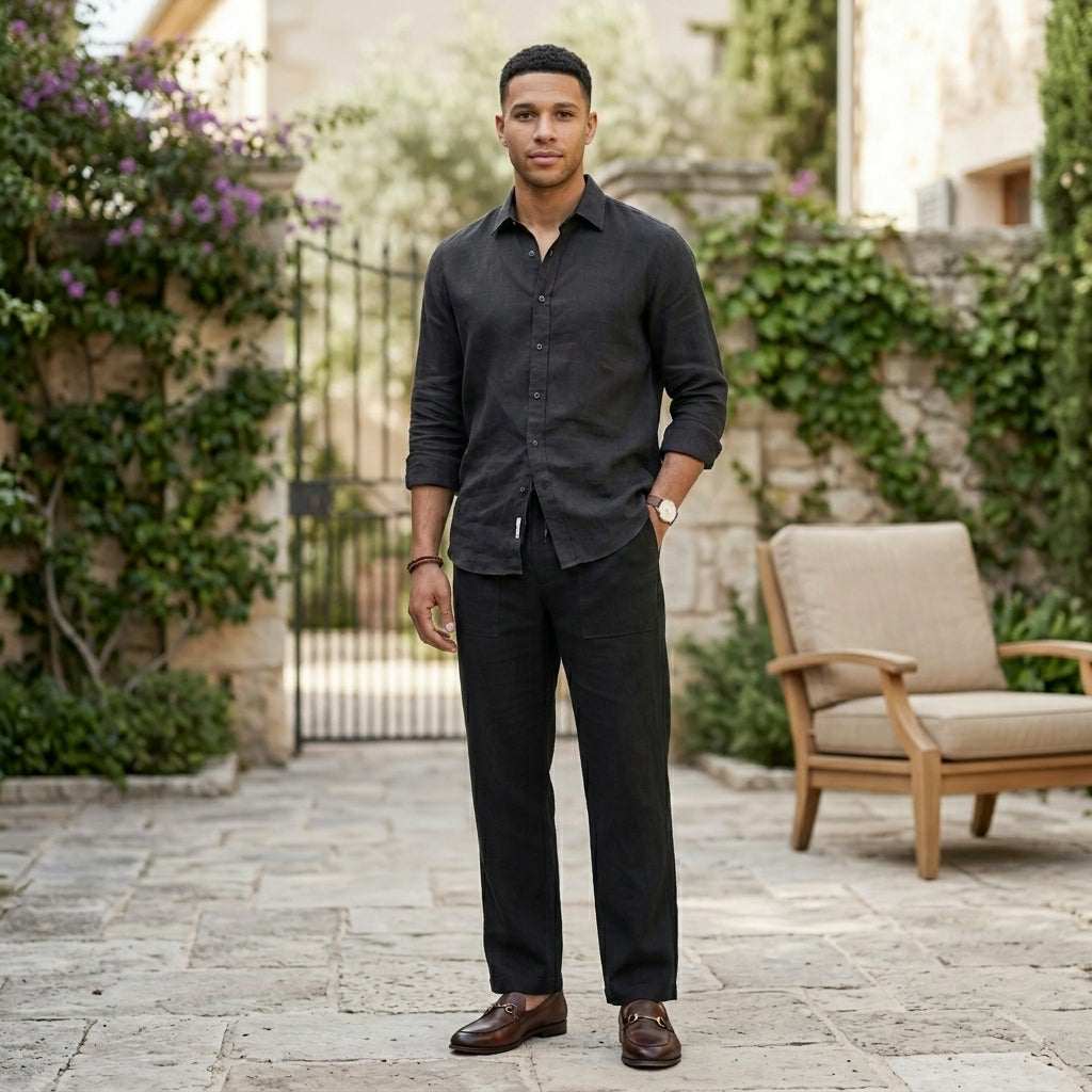 Male model wearing black relaxed-fit casual pants with a black long-sleeve shirt in an outdoor stone walkway setting.