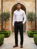 Male model wearing black tailored dress pants with a white long-sleeve shirt in an outdoor courtyard setting.