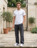 Male model wearing charcoal gray relaxed-fit casual pants with a white T-shirt in an outdoor walkway setting.