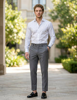 Male model wearing gray pleated tailored pants with a white long-sleeve shirt in an outdoor walkway setting.