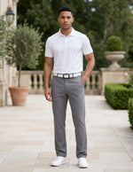 Male model wearing gray tailored casual pants with a white short-sleeve polo shirt in an outdoor garden walkway setting.