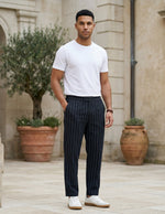 Male model wearing navy pinstripe relaxed-fit pants with a white T-shirt in an outdoor stone walkway setting.