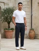Male model wearing navy pinstripe relaxed-fit pants with a white T-shirt in an outdoor stone walkway setting.