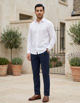 Male model wearing navy tailored pants with a white long-sleeve shirt in an outdoor stone walkway setting.