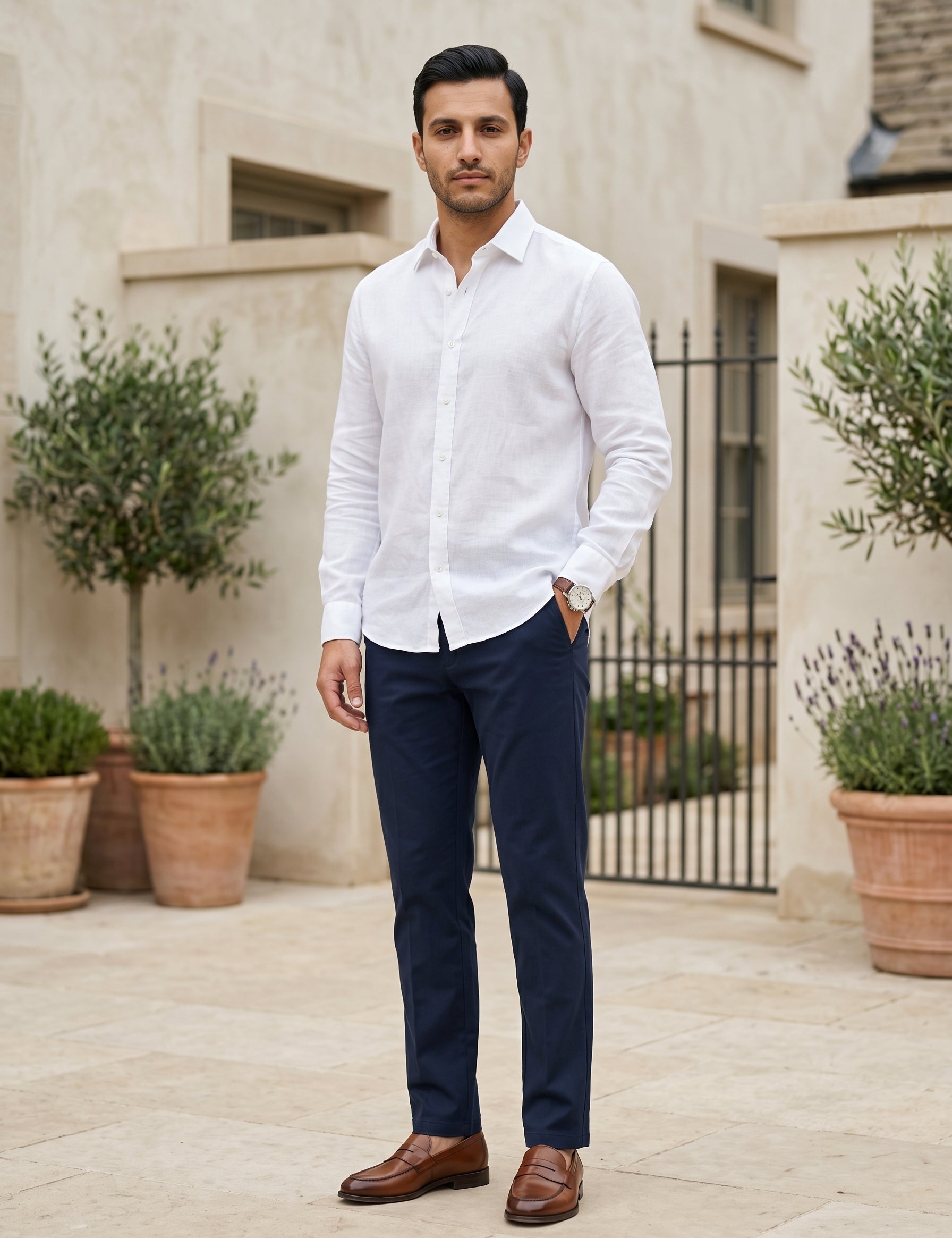 Male model wearing navy tailored pants with a white long-sleeve shirt in an outdoor stone walkway setting.