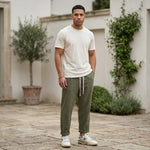 Male model wearing olive green drawstring jogger pants with a beige T-shirt in an outdoor stone walkway setting.