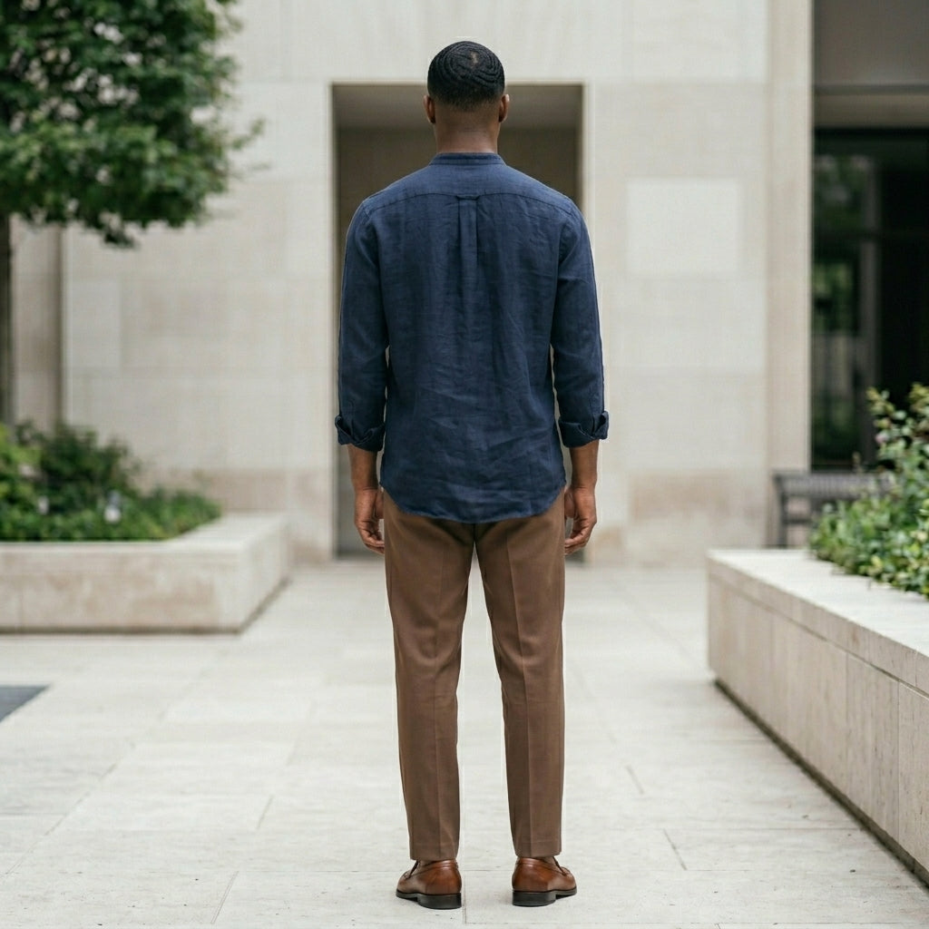 Man in a blue shirt and brown pants walking away from the camera in an outdoor setting.