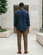 Man in a blue shirt and brown pants walking away from the camera in an outdoor setting.