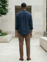 Man in a blue shirt and brown pants walking away from the camera in an outdoor setting.