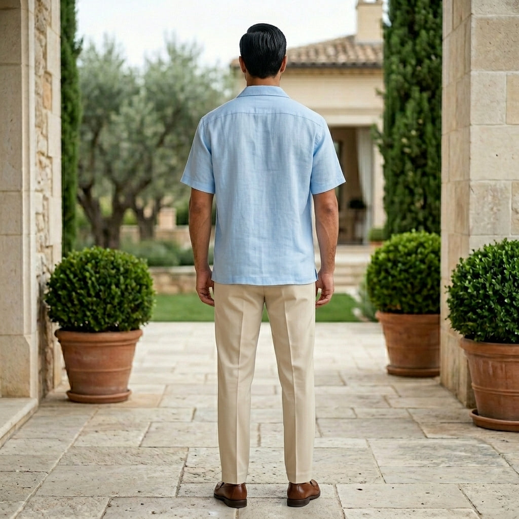 Man in a light blue shirt and beige pants walking away from the camera in a garden setting.