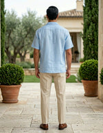 Man in a light blue shirt and beige pants walking away from the camera in a garden setting.