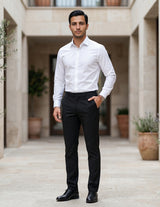 Man in a white shirt and black pants standing in an outdoor setting with plants.