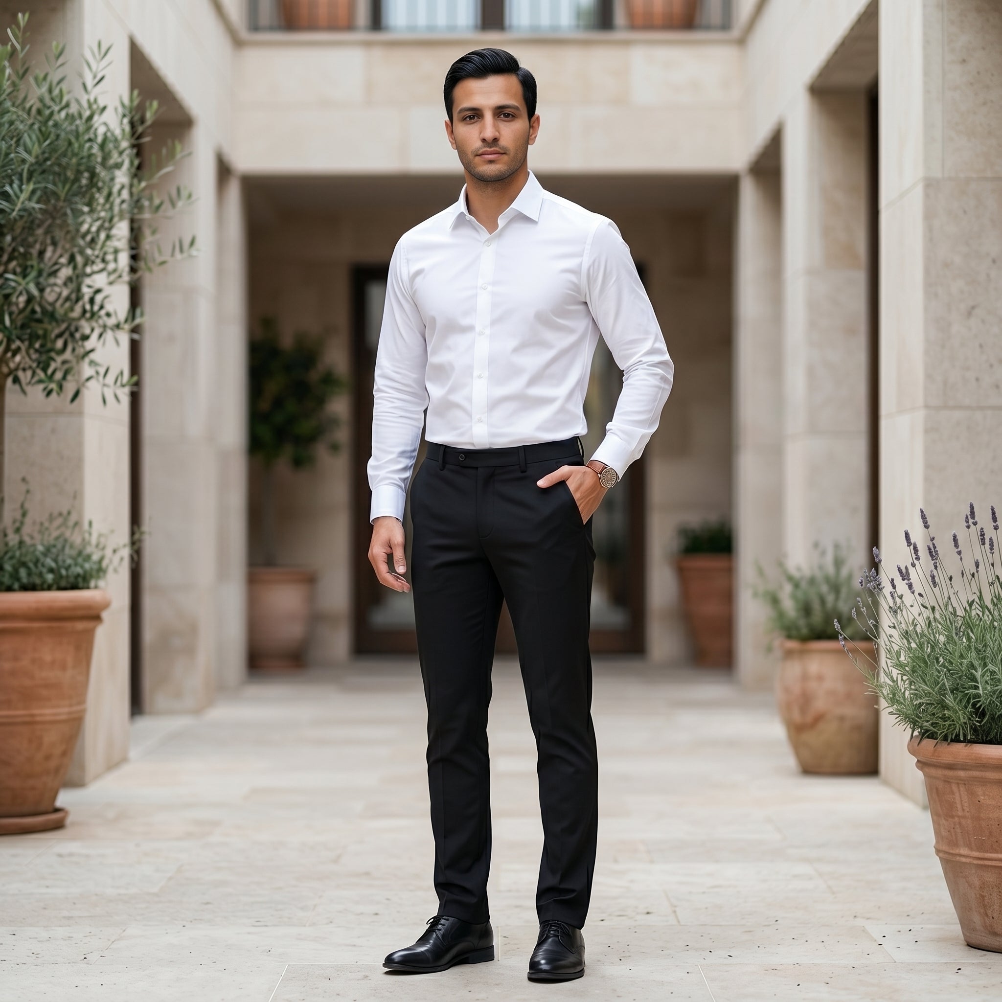 Man in a white shirt and black pants standing in an outdoor setting with plants.