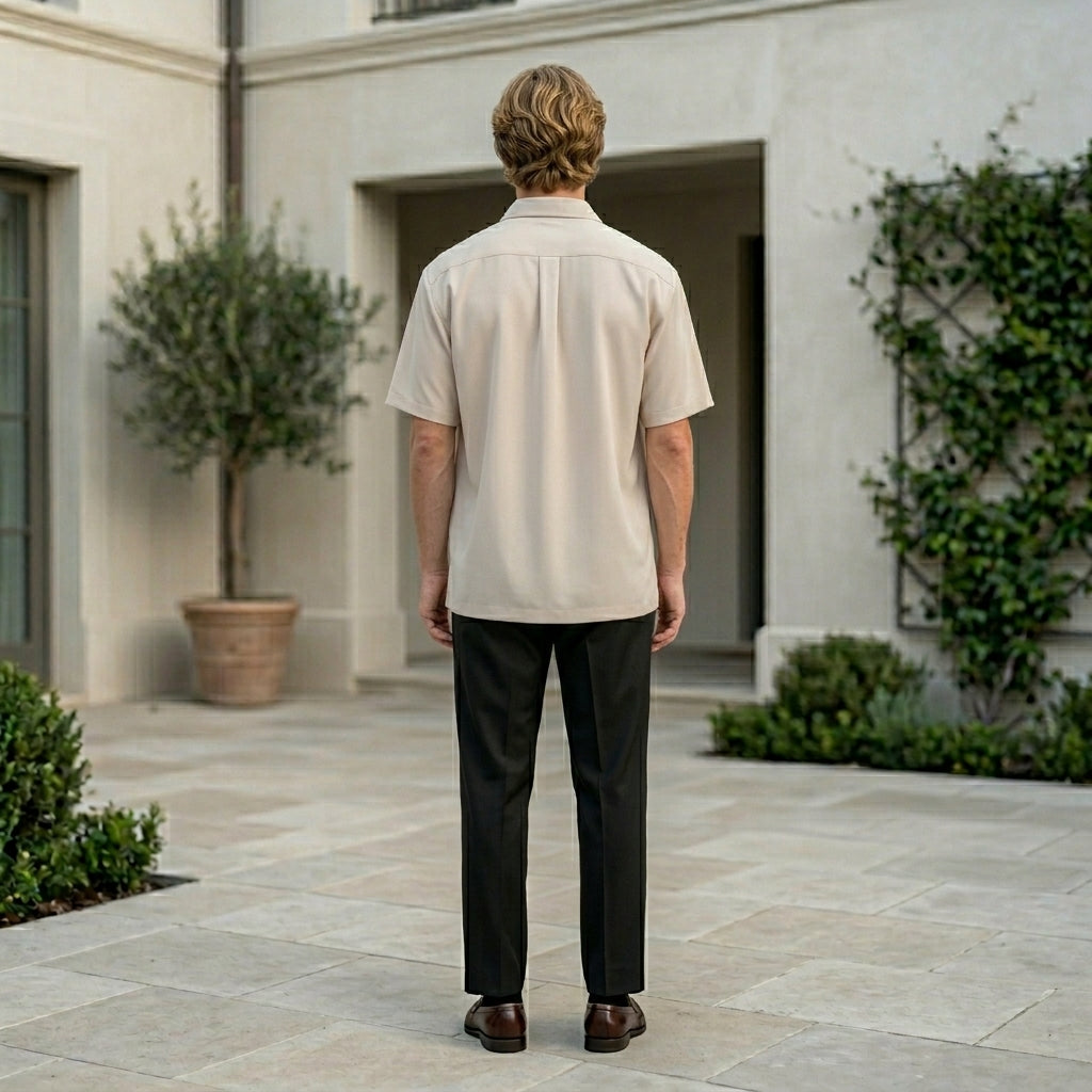 Man standing in a courtyard wearing a beige shirt and dark pants.