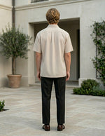 Man standing in a courtyard wearing a beige shirt and dark pants.