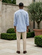 Man standing outdoors wearing a light blue shirt and beige pants.